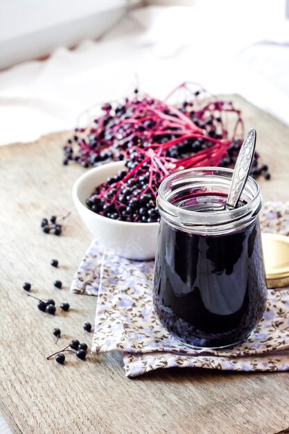 Homemade black elderberry syrup in glass jar and bunches of black elderberry