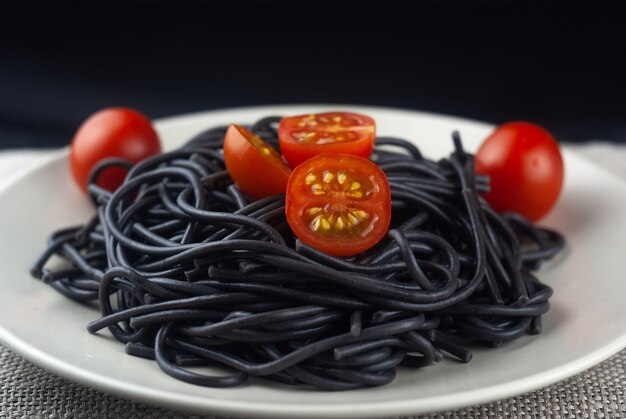 Homemade black pasta with tomatoes on the red dish. Cooked black macaroni