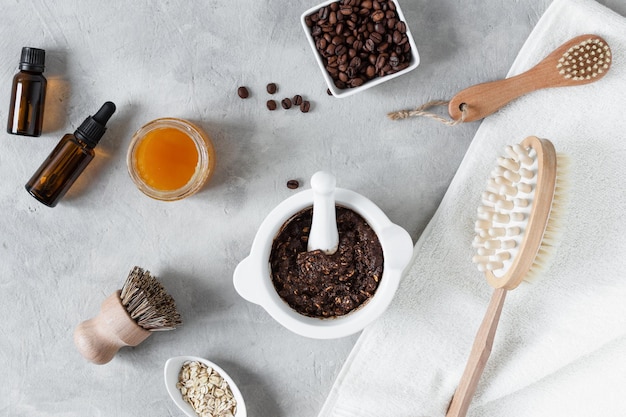 Scrub per il corpo fatto in casa con miele di caffè macinato e farina d'avena in un barattolo su un tavolo di cemento grigio