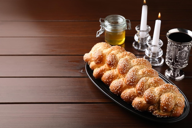 Homemade braided bread with sesame seeds goblet honey and candles on wooden table space for text Traditional Shabbat challah