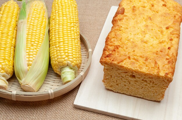 Homemade brazilian corn bread on a cutting board and raw corn cobs in a woven bamboo basket