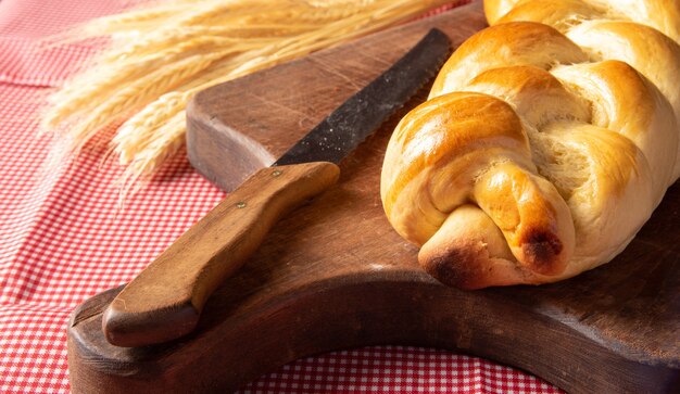 Homemade bread, braided bread on wood and a red and white checkered tablecloth, a knife and a branch of wheat.