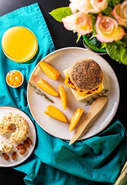 Homemade breakfast: sandwich with cheese and ham, cream cheese, almond, persimmon, jam and orange juice. Top view, flat-lay