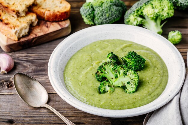 Homemade broccoli cream soup in white bowl with toasts on wooden rustic background