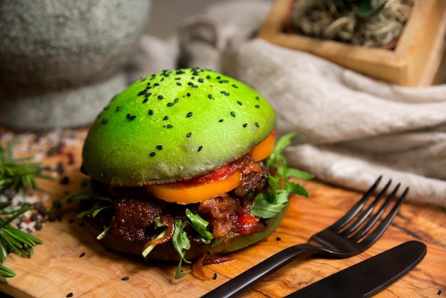 Homemade burger, green bun with orange tomato, onions, arugula, grilled meat, black sesame seeds