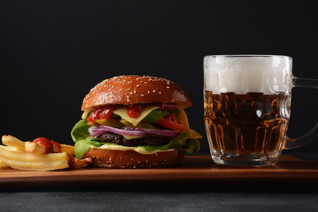 Homemade burger with grilled beef, cheese, onion, tomato, and\
green salad, sauce, with pickles and french fries,and a glass of\
beer in the background.