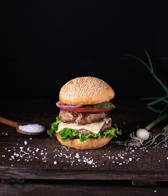 Homemade burger with lettuce, cheese, onion and tomato on a rustic wooden board