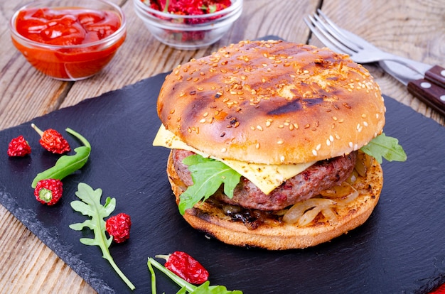 Homemade burger with sesame bun and ground beef on black stone. 