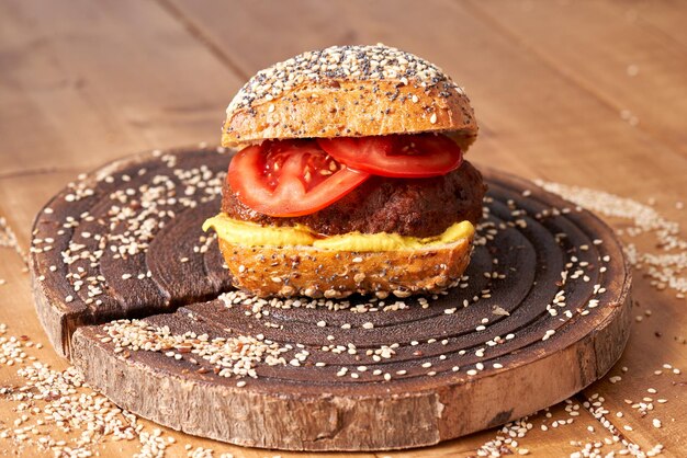 Homemade burger with tomatoes and mustard on the wooden table.