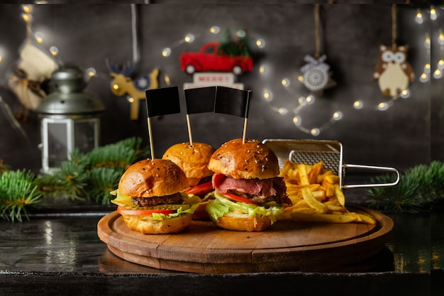 Hamburger e patatine fritte fatti in casa su tavola di legno con decorazioni natalizie sul muro, vista del primo piano