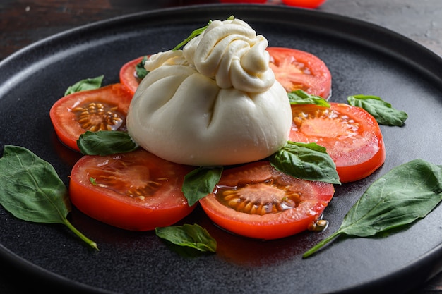 Burrata fatta in casa servita con pomodori freschi e foglie di basilico