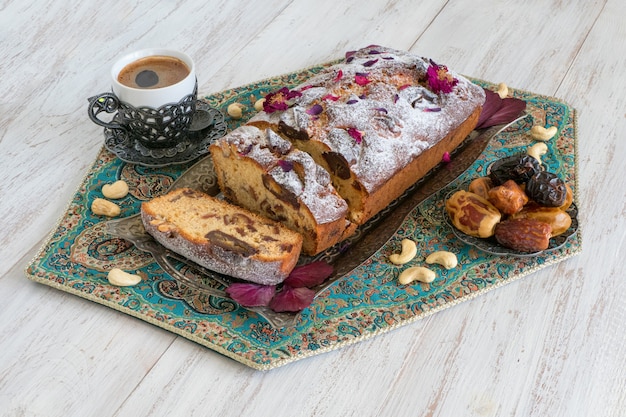 Homemade cake with dates and nuts, served with black coffee on a white wooden table