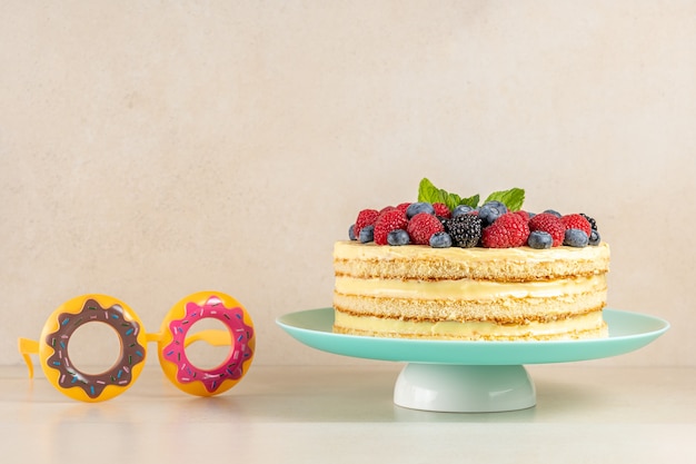 Домашний торт со свежими ягодами и партийными очками на ярком фоне.