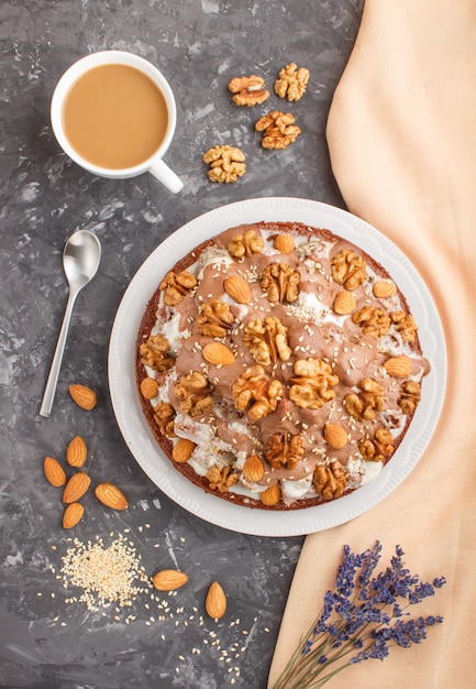 Homemade cake with milk cream, cocoa, almond, hazelnut on black concrete with orange textile and a cup of coffee. Top view, copy space.