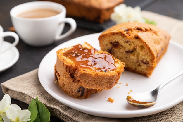 Homemade cake with raisins, almonds, soft caramel and a cup of coffee on a black concrete background and linen textile. Side view, close up, selective focus.