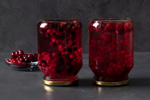 Homemade canned compote with cherries and currants in two jars on a dark gray background.