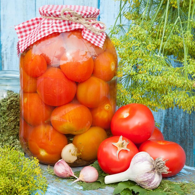 ガラスの瓶に自家製缶詰のトマト木の板に新鮮な野菜のディルとニンニク