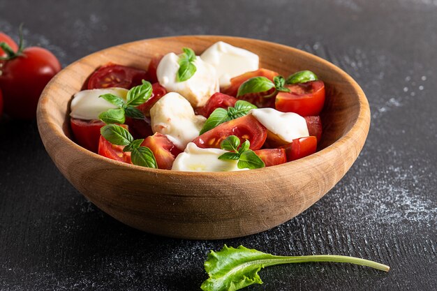 Homemade caprese salad in wooden bowl on black background close up. Traditional Italian dish.