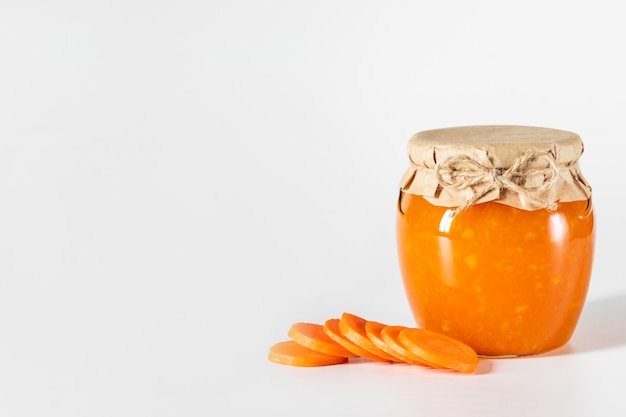 Homemade carrot jam in glass jar on a white background