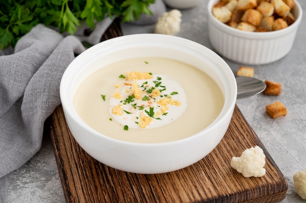 Purea di zuppa di cavolfiore fatta in casa in una ciotola bianca con spezie crema di formaggio e prezzemolo fresco o