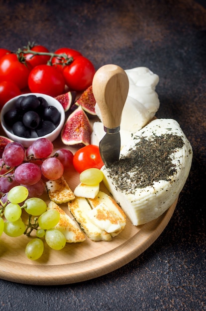 Homemade cheese for frying halloumi with mint on wooden board. Traditional Greek or Cyprus cheese on dark background with tomatoes pepper, olives, grapes, figs and herb