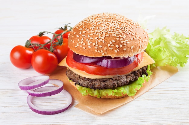 Homemade cheeseburger with beef patties, fresh salad, tomatoes and onion on seasame buns, served on white wooden table.