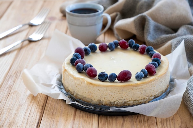 Homemade cheesecake decorated with blueberry and cranberry on parchment with coffee cup and forks on background Festive dessert pastry