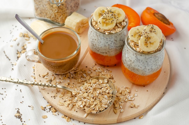 Homemade chia seed pudding with banana, smashed fresh apricot and oat meals and coffee on wooden board with copy space.