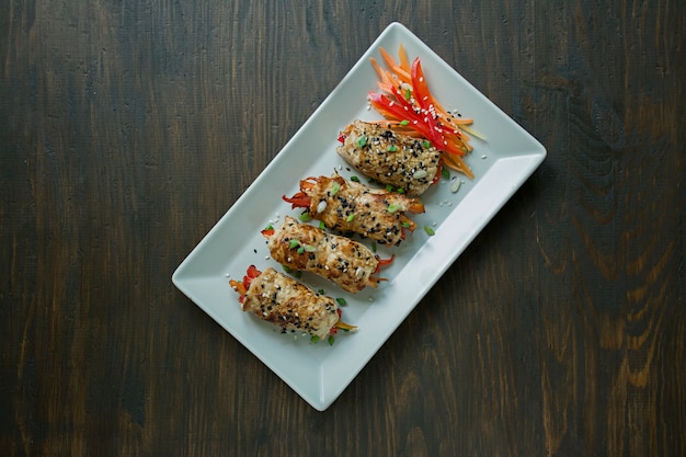 Homemade chicken breast rolls with greens, carrot slices, bell pepper on a light rectangular plate