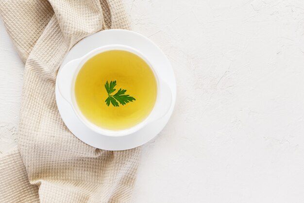 Homemade chicken broth in a white plate on a white table