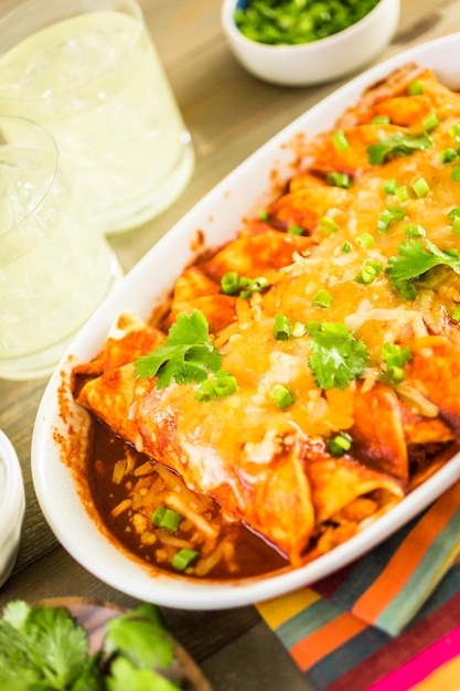 Homemade chicken enchiladas garnished with green onions and cilantro in a white casserole dish.