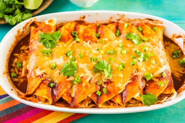 Homemade chicken enchiladas garnished with green onions and cilantro in a white casserole dish.