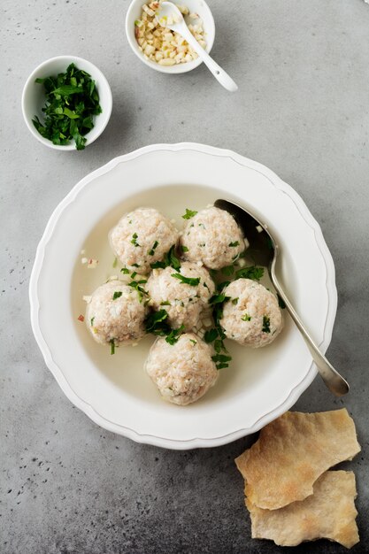 Zuppa di polpette di pollo matzo fatta in casa con prezzemolo e aglio in un semplice piatto di ceramica bianca su una pietra grigia o cemento