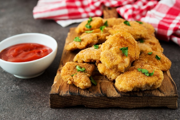 Homemade chicken nuggets with herbs and ketchup on a wooden board