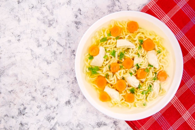 Homemade chicken soup with noodles and vegetables in a white bowl on a gray background