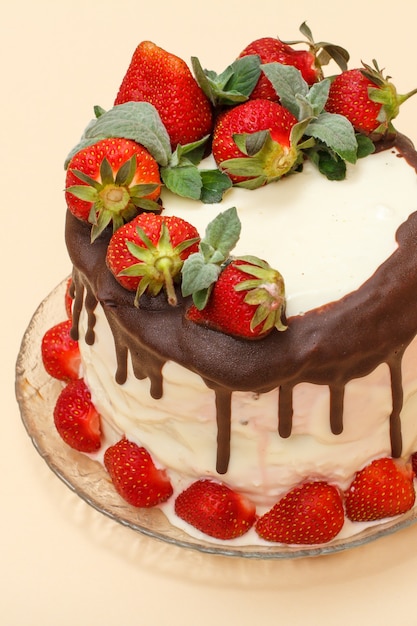 Homemade chocolate cake decorated with fresh strawberries on glass plate on beige color background with copy space