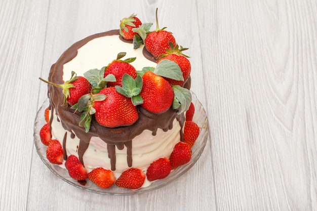 Homemade chocolate cake decorated with fresh strawberries on glass plate with grey wooden background and copy space