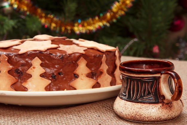 Foto torta al cioccolato fatta in casa decorata con ornamenti e tazza di caffè sul tavolo con albero di natale sullo sfondo.