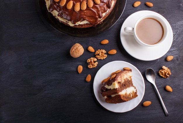 Homemade chocolate cake with milk cream, caramel and almonds on blackwoodcup of coffee.