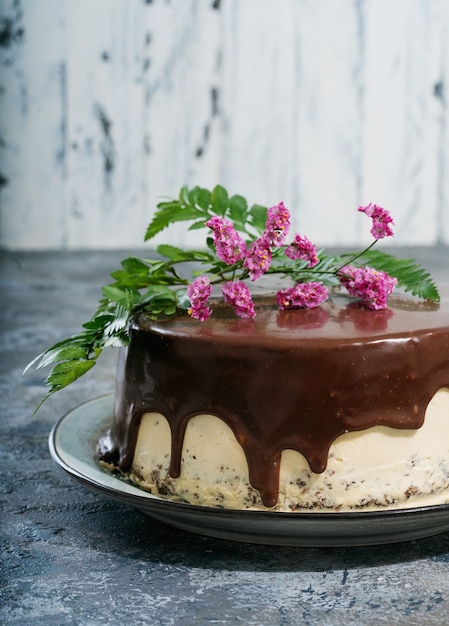 Homemade chocolate cake with peanut butter cream layers decorated with flowers on the top over a dark rustic desk. Side view.