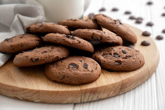 Homemade chocolate chip cookies on wooden board with glass of milk and kitchen towel Recipe of delicious dessert for tea freshly baked cookies with chocolate crumbs