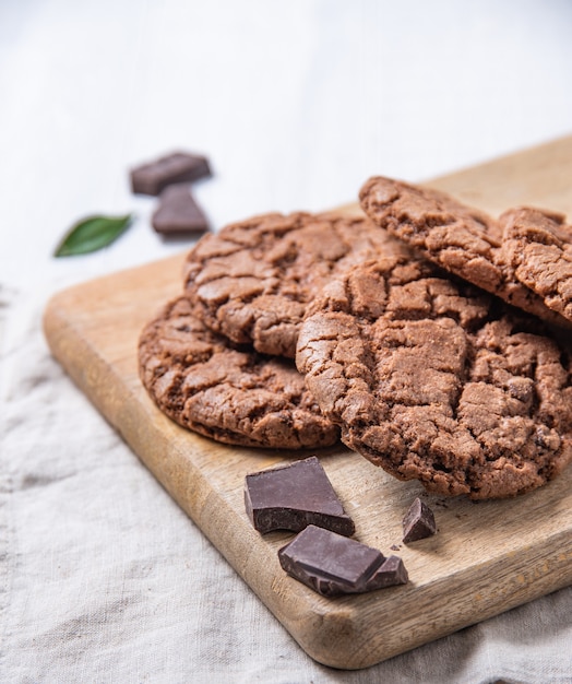 Photo homemade chocolate cookies with chocolate chips on wood cutting board  on a light table. front view and copy space