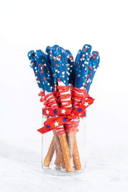 Homemade chocolate-covered pretzel rods decorated like the American flag in a glass jar.