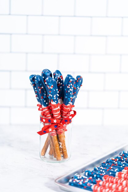 Homemade chocolate-covered pretzel rods decorated like the\
american flag in a glass jar.