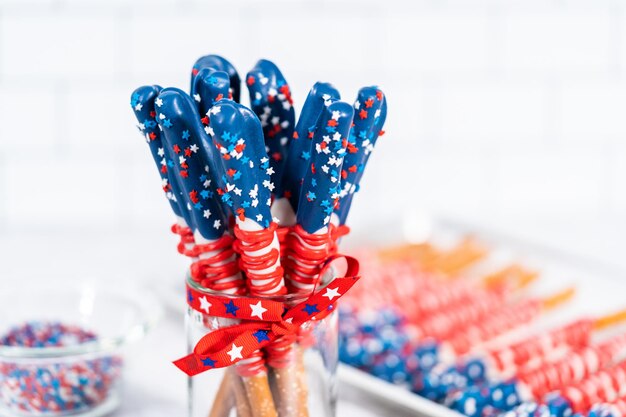 Homemade chocolate-covered pretzel rods decorated like the\
american flag in a glass jar.