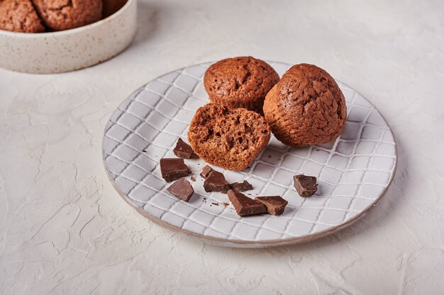 Homemade chocolate cupcakes and pieces of chocolate in textured plate on wooden light background top