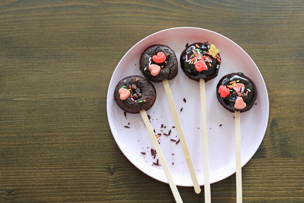 Homemade chocolate donut with topping on plate against wooden table.