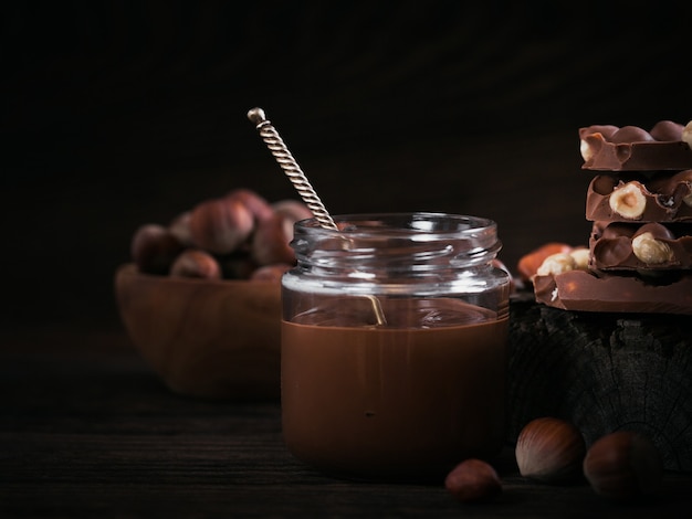 ダークウッドの背景のガラス瓶に自家製チョコレートヘーゼルナッツミルクスプレッド