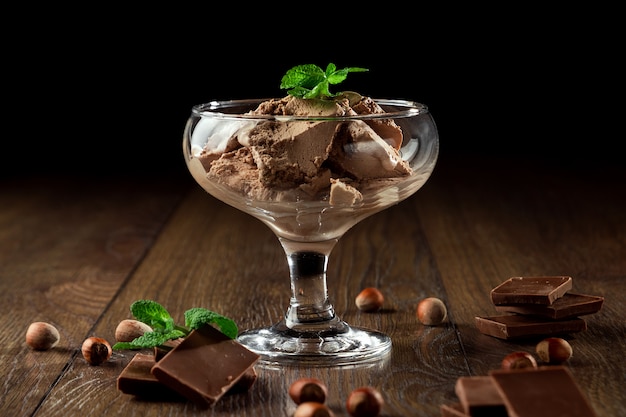 Homemade chocolate ice cream with mint leaves, sprinkled with chocolate in a glass bowl on a wooden table