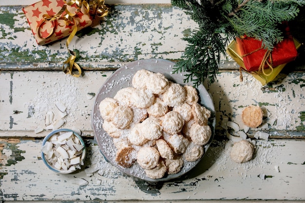 Biscotti senza glutine fatti in casa di cocco di natale con fiocchi di cocco sul piatto in ceramica sul vecchio tavolo in legno con decorazioni e regali di natale. lay piatto